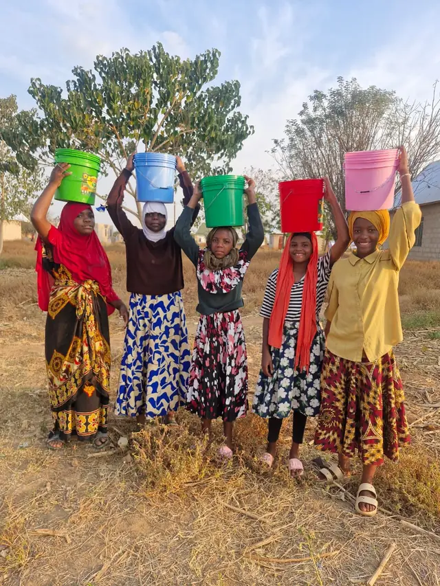 Girls carrying colourful water buckets on their heads
